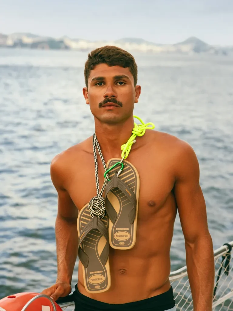 Hombre con ojotas colgadas del cuello frente al mar